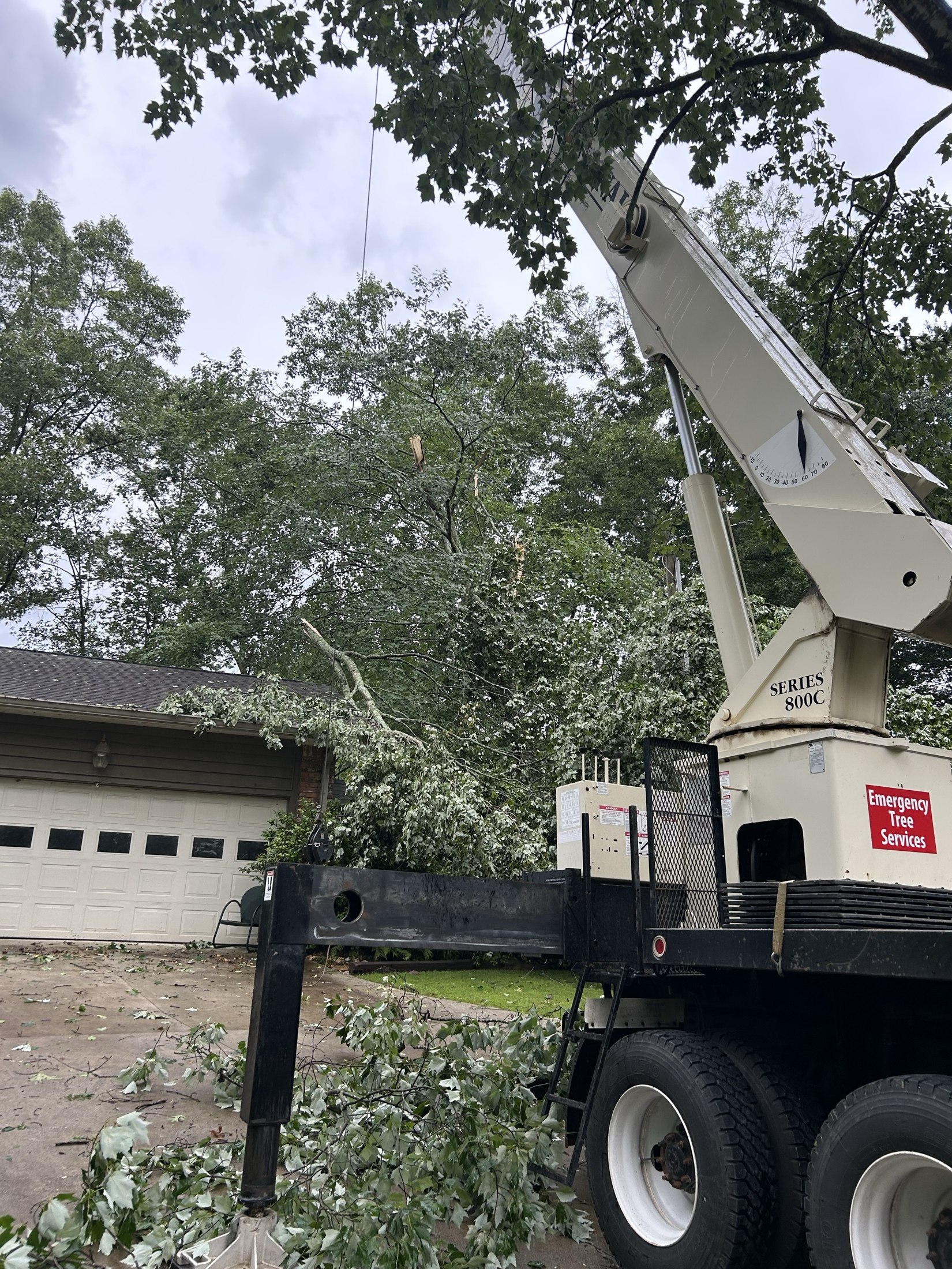 A crane positioned beside a garage with a fallen tree across the roof and branches on the driveway